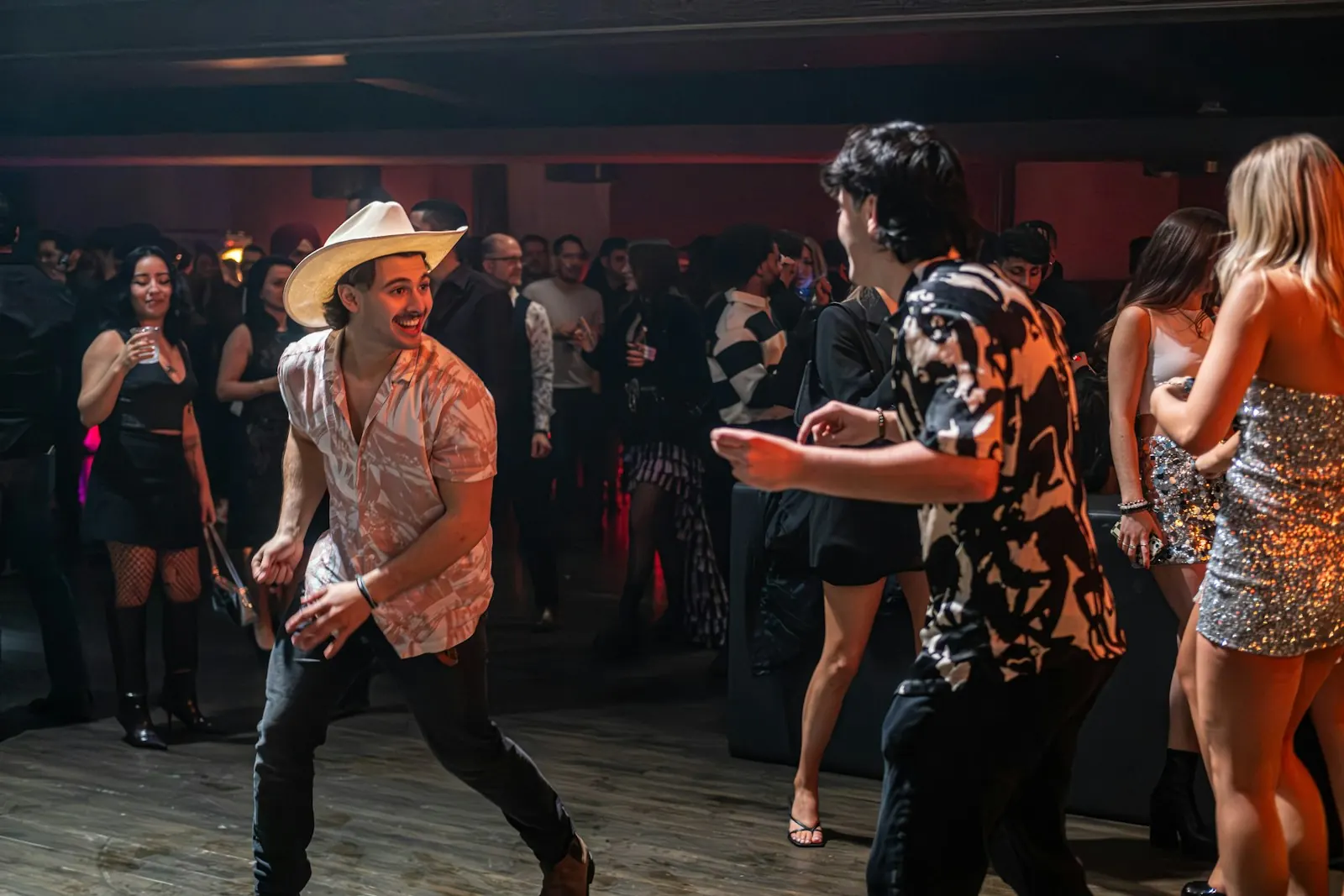 Un gars en chapeau de cowboy qui danse avec ses amis dans un bar